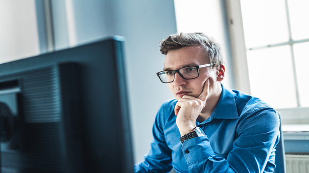 Handsome Young Businessman Wearing Eyeglasses Sitting At His Table Inside The Office, Looking At The stock photo